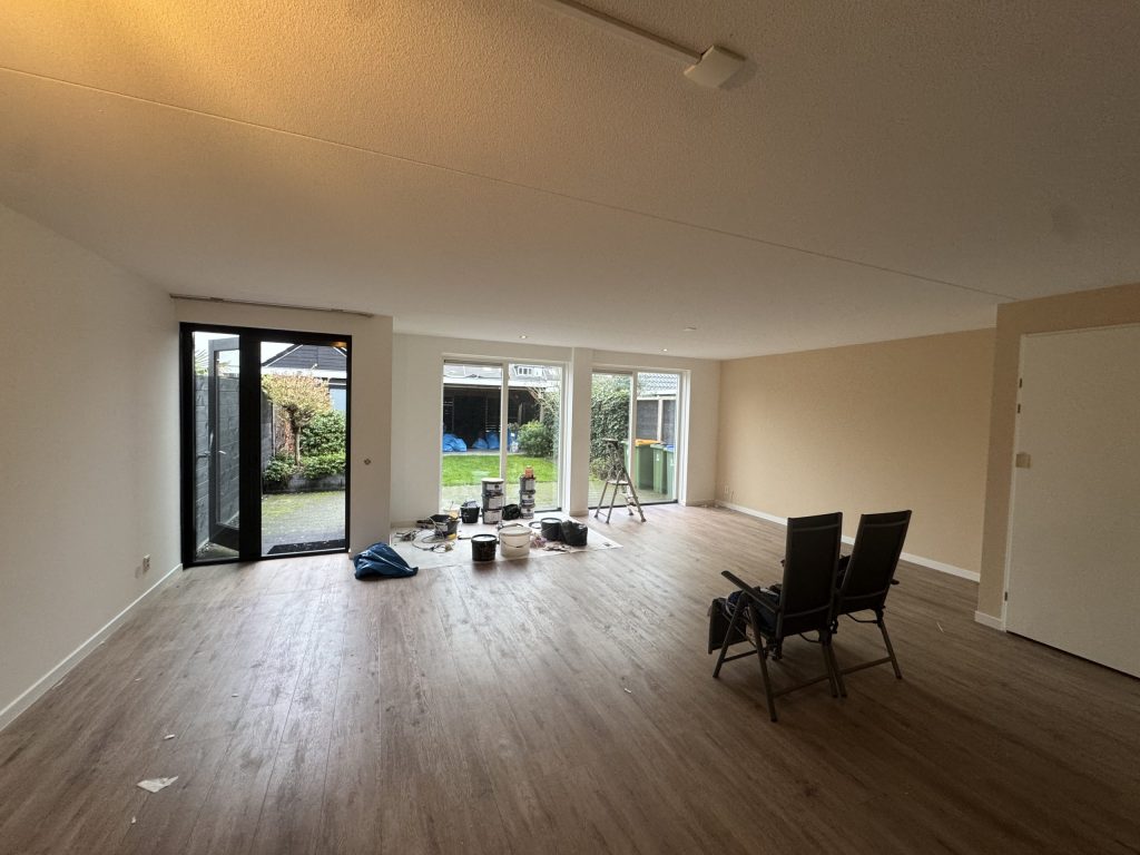 Ruime woonkamer van een bestaand rijtjeshuis met lichte wanden, een houten vloer en tuindeuren