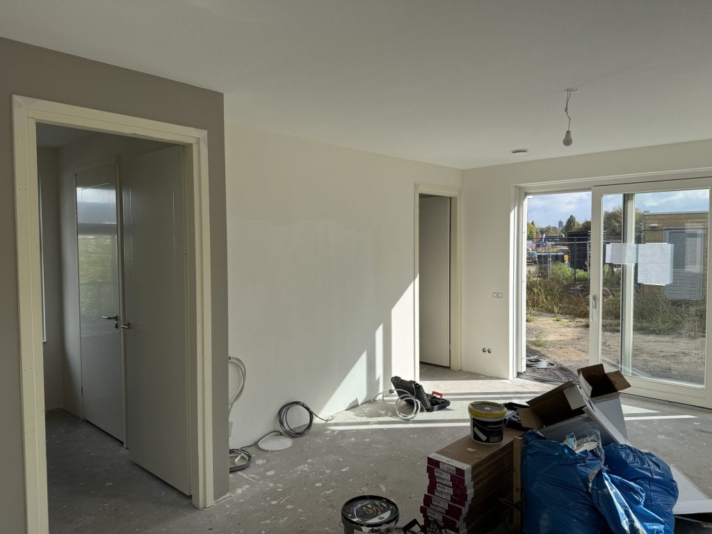 Nieuwbouwwoonkamer tijdens de afwerking met open binnendeuren, schuifpui en emmers verf op de betonvloer